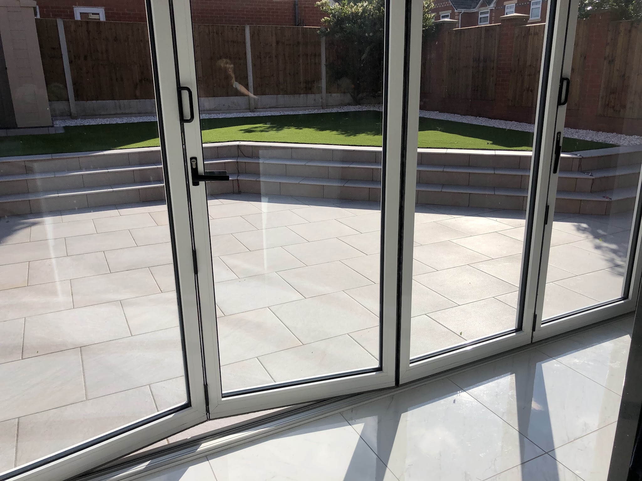 A pale smooth patio and stepped lawn seen through open bi-fold doors