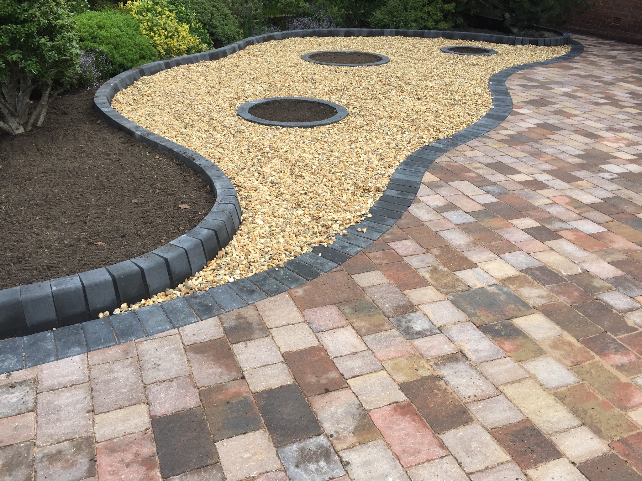 Mixed-colour block paving curving round a gravel bed with dark kerb edging