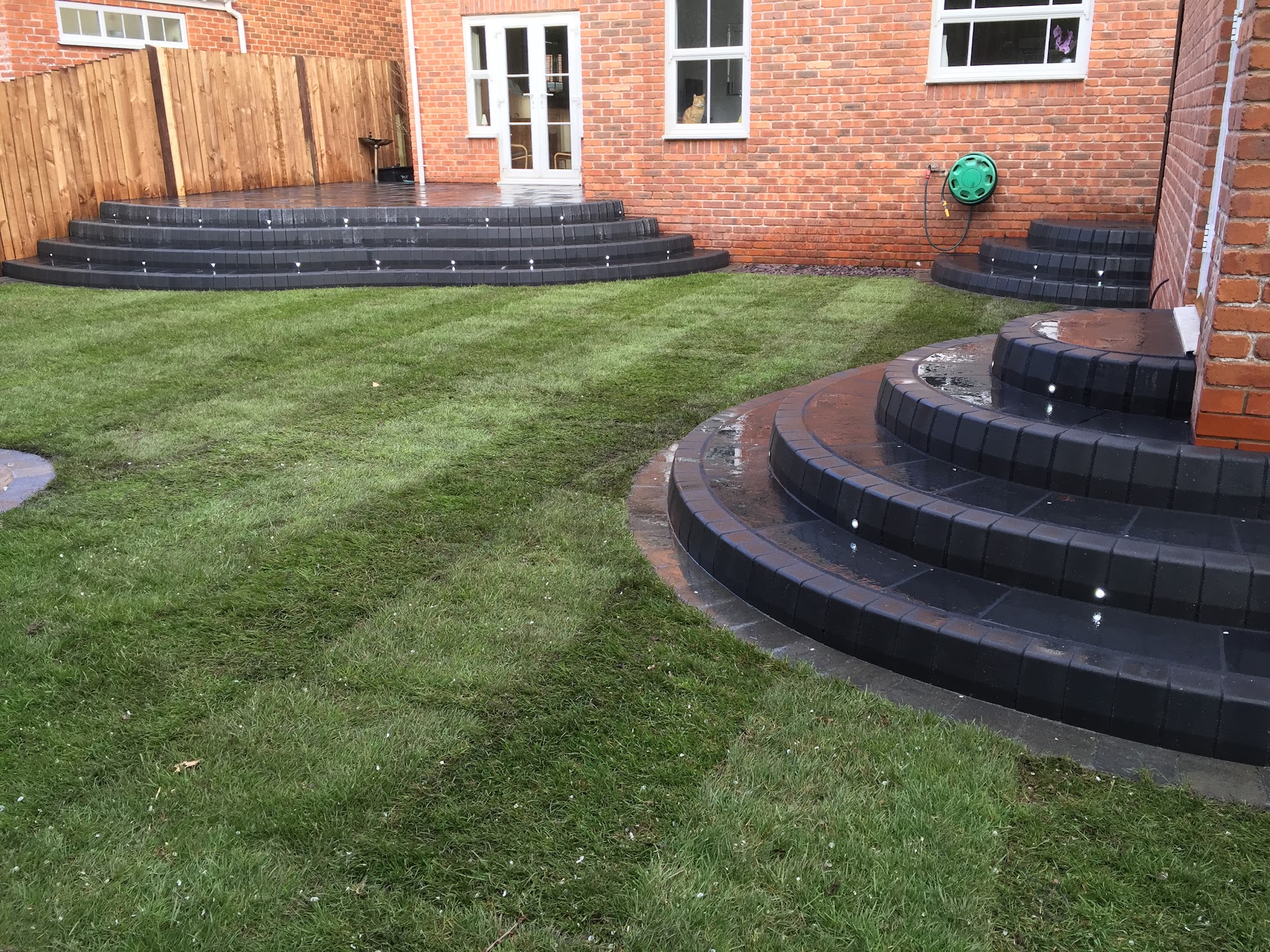 Dark curved garden steps with built-in lights beside a freshly striped lawn