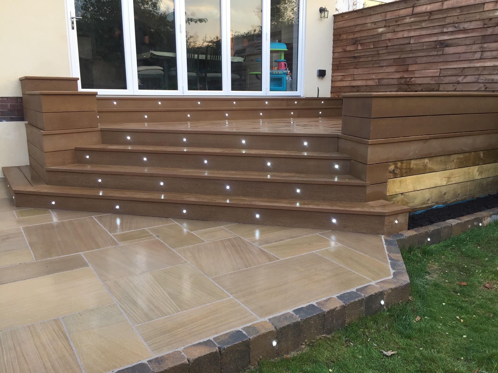 Timber-effect deck steps with built-in lights beside buff paving