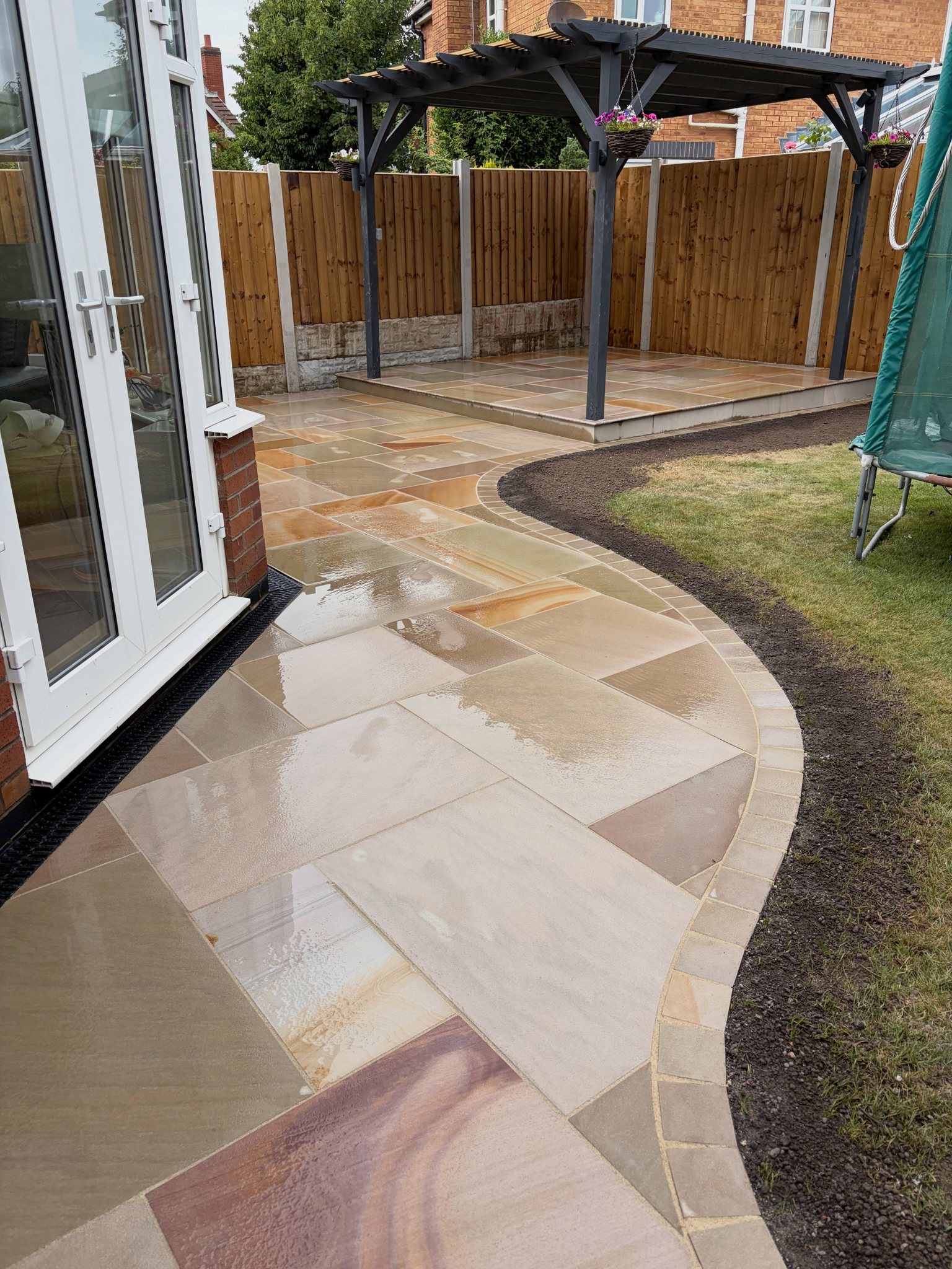 A curved buff stone path leading to a timber pergola